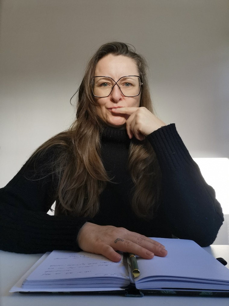 Sandra Laudenbach mit Brille am Schreibtisch, Hand auf dem Notizbuch